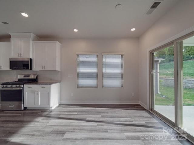 kitchen with light wood-type flooring, recessed lighting, white cabinets, tasteful backsplash, and stainless steel appliances