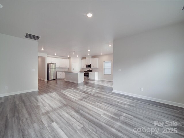 unfurnished living room featuring visible vents, recessed lighting, light wood-style floors, and baseboards