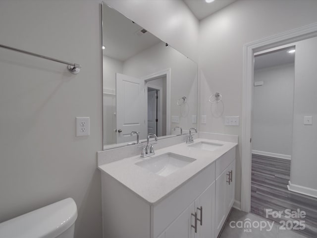 bathroom with double vanity, a sink, baseboards, and toilet