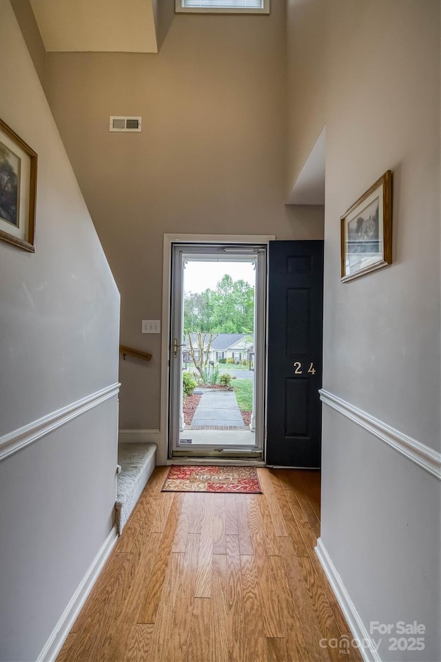 entryway with baseboards, visible vents, wood finished floors, and a towering ceiling