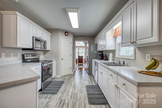 kitchen featuring white cabinetry, a sink, light wood-style floors, stainless steel appliances, and light countertops