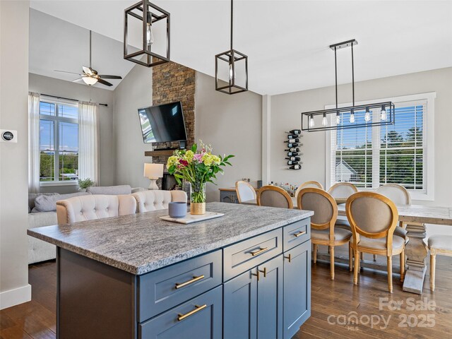 kitchen with a ceiling fan, open floor plan, decorative light fixtures, dark wood-style flooring, and a kitchen island