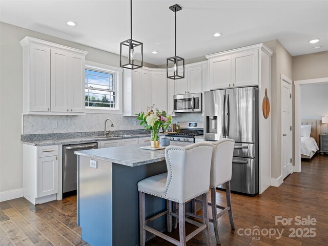 kitchen with stainless steel appliances, a sink, dark wood-type flooring, a kitchen bar, and tasteful backsplash