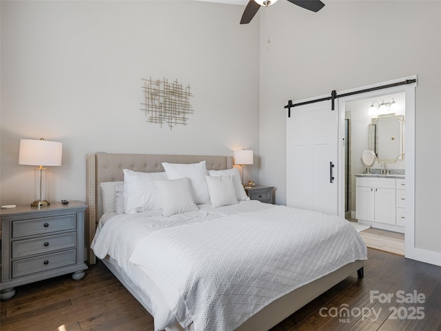 bedroom featuring a barn door, wood finished floors, a high ceiling, ceiling fan, and ensuite bath