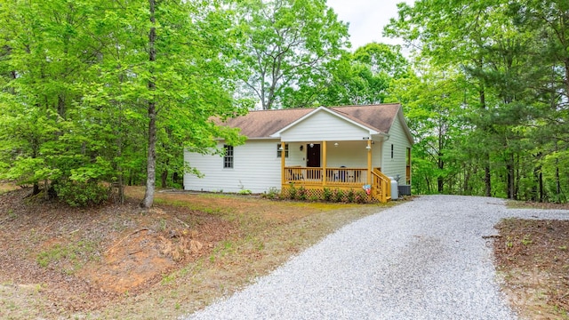 view of front of home featuring covered porch, a shingled roof, and gravel driveway