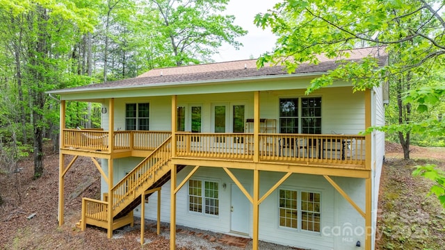 rear view of property with a deck, stairs, and roof with shingles