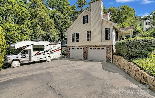 view of side of home featuring a chimney, a garage, driveway, and stone siding