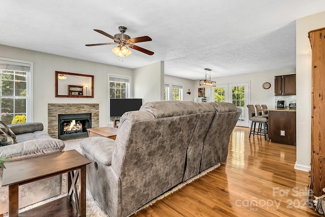 living room with light wood-style floors, a ceiling fan, a textured ceiling, and a stone fireplace