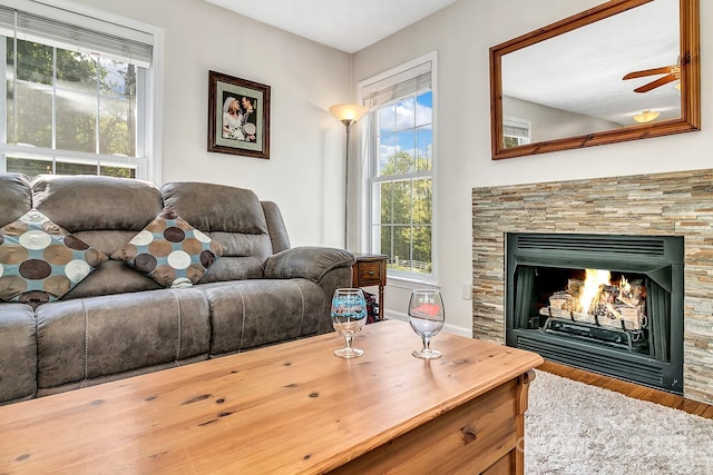 living room with a ceiling fan, plenty of natural light, wood finished floors, and a fireplace