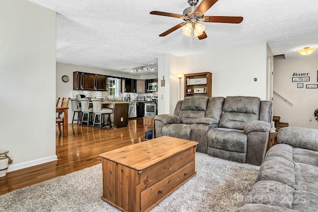 living area with baseboards, a textured ceiling, ceiling fan, and wood finished floors