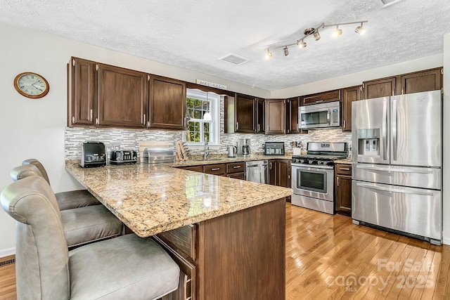 kitchen featuring a peninsula, dark brown cabinetry, light stone counters, light wood finished floors, and stainless steel appliances