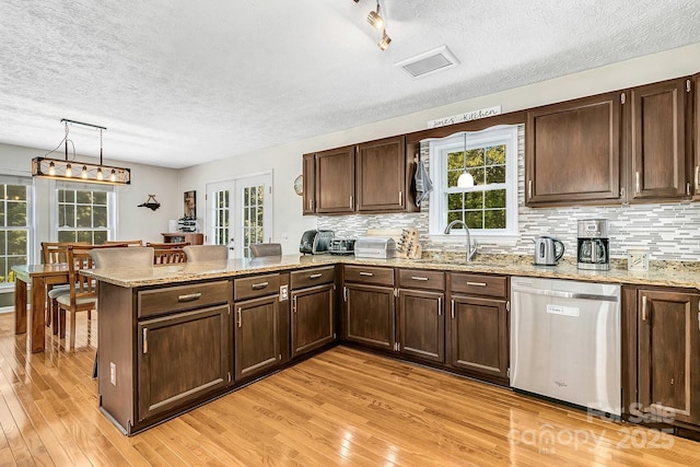 kitchen featuring stainless steel dishwasher, a sink, light wood-style floors, and a peninsula