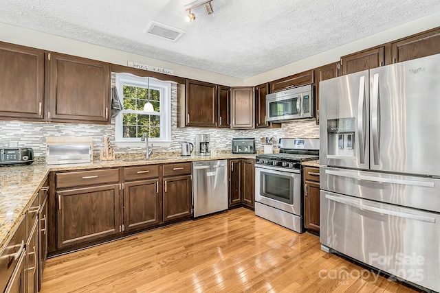 kitchen with a textured ceiling, appliances with stainless steel finishes, a sink, and light wood-style flooring