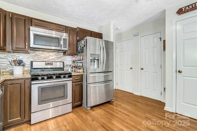 kitchen featuring dark brown cabinets, light wood-type flooring, light stone counters, backsplash, and stainless steel appliances