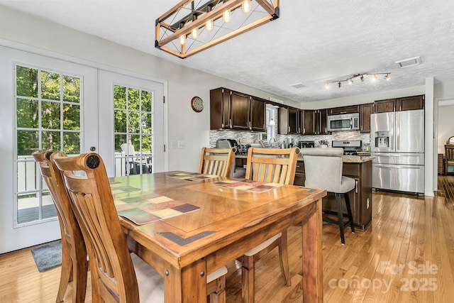 dining space with a textured ceiling, light wood-style flooring, and visible vents