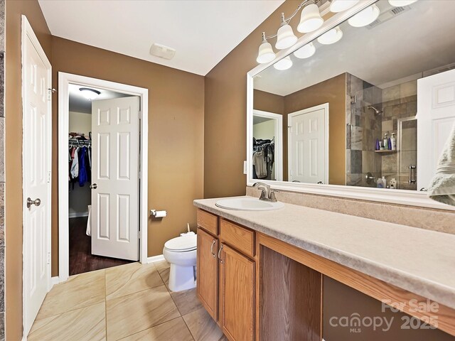 full bathroom with toilet, vanity, a walk in closet, baseboards, and a stall shower