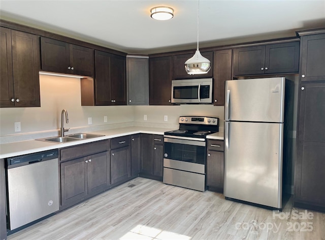 kitchen featuring stainless steel appliances, a sink, dark brown cabinets, light wood-style floors, and light countertops