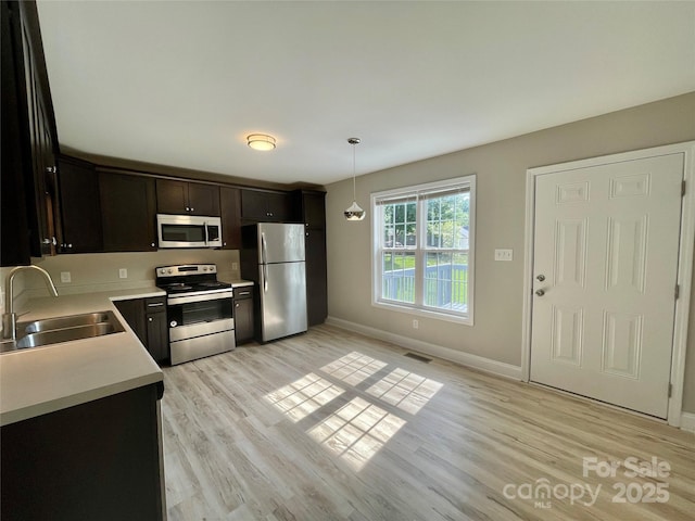 kitchen featuring appliances with stainless steel finishes, a sink, light wood-type flooring, light countertops, and baseboards