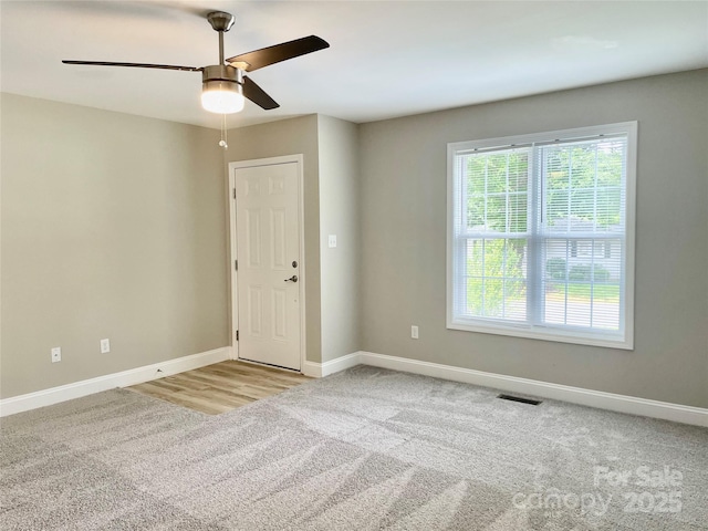 carpeted spare room with healthy amount of natural light, a ceiling fan, and baseboards
