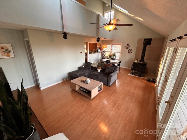 living area with high vaulted ceiling, ceiling fan, a wood stove, and wood finished floors