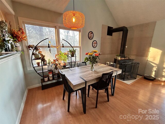 dining room featuring lofted ceiling, wood finished floors, a wood stove, and baseboards