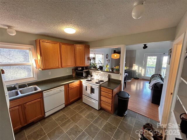 kitchen featuring dark countertops, a sink, brown cabinets, white appliances, and french doors