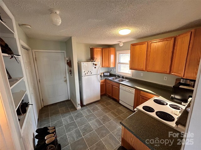 kitchen with dark countertops, a sink, white appliances, and a textured ceiling
