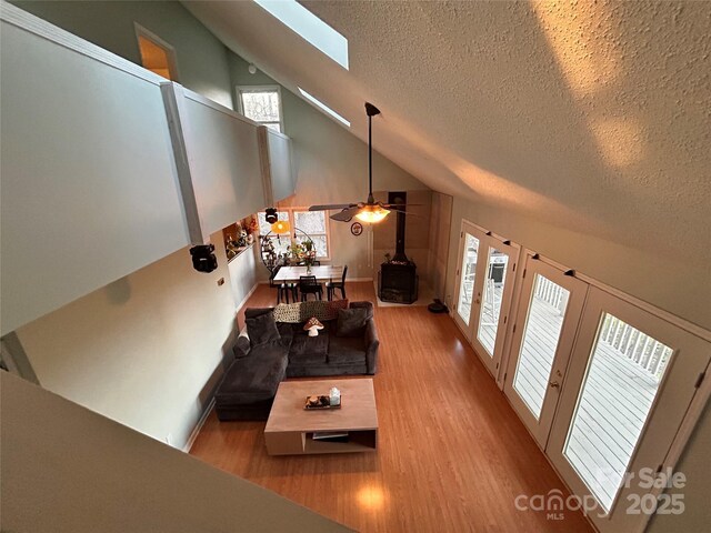 living room featuring a skylight, wood finished floors, high vaulted ceiling, and a wood stove