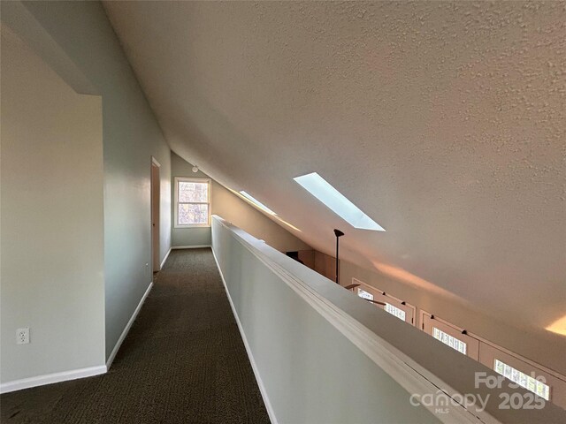 corridor featuring baseboards, vaulted ceiling with skylight, a textured ceiling, and carpet floors