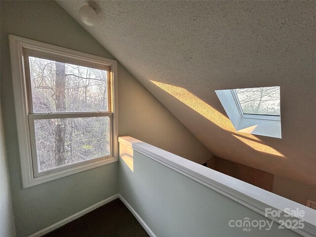 bonus room featuring plenty of natural light, baseboards, a textured ceiling, and vaulted ceiling with skylight