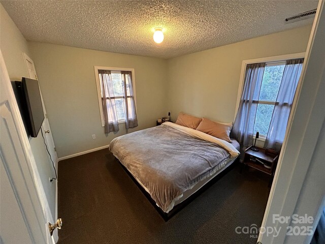 bedroom with a textured ceiling, visible vents, dark carpet, and baseboards