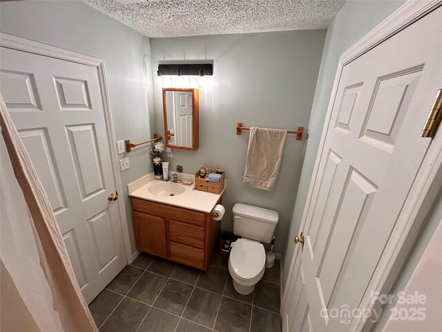 bathroom with a textured ceiling, tile patterned floors, vanity, and toilet