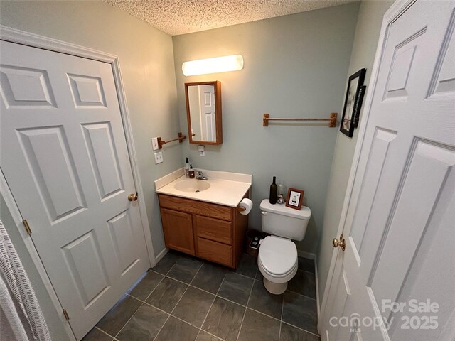 half bathroom featuring tile patterned flooring, toilet, vanity, and a textured ceiling