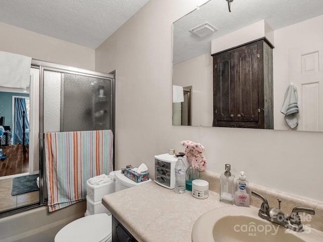 125 Snug Harbor Cir, Lake Lure, NC 28746 - bathroom featuring toilet, vanity, a textured ceiling, visible vents, and shower / bath combination with glass door