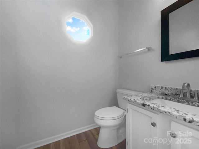 half bathroom featuring baseboards, wood finished floors, toilet, and vanity