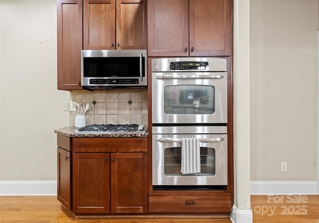 860 Arrow Point Ln, Davidson, NC 28036 - kitchen featuring dark stone counters, stainless steel appliances, light wood-style floors, tasteful backsplash, and baseboards