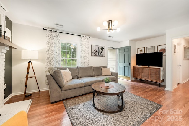 living room featuring light wood-style floors, baseboards, a notable chandelier, and visible vents