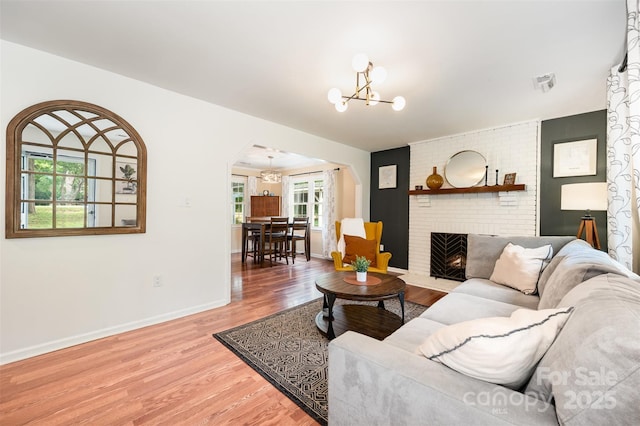 living room with an inviting chandelier, a brick fireplace, arched walkways, baseboards, and light wood-type flooring