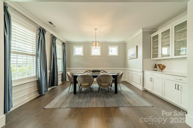 dining space featuring visible vents, ornamental molding, dark wood finished floors, and a wainscoted wall