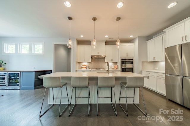 kitchen featuring a breakfast bar area, appliances with stainless steel finishes, tasteful backsplash, a sink, and wine cooler