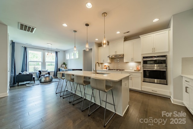 kitchen with a breakfast bar area, stainless steel double oven, visible vents, a sink, and under cabinet range hood