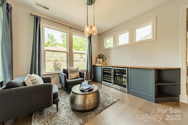 sitting room with wine cooler, a dry bar, light wood-type flooring, and visible vents