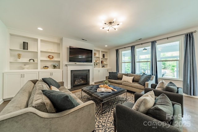 living area featuring visible vents, built in features, wood finished floors, and a glass covered fireplace
