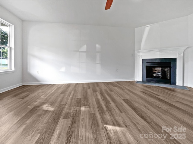 unfurnished living room with a fireplace with flush hearth, baseboards, a ceiling fan, and wood finished floors