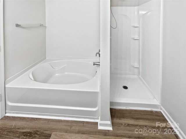 bathroom with a garden tub, walk in shower, and wood finished floors