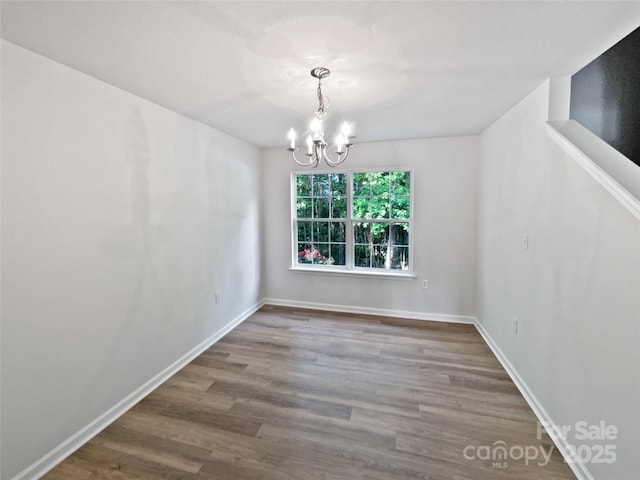 unfurnished dining area featuring an inviting chandelier, wood finished floors, and baseboards