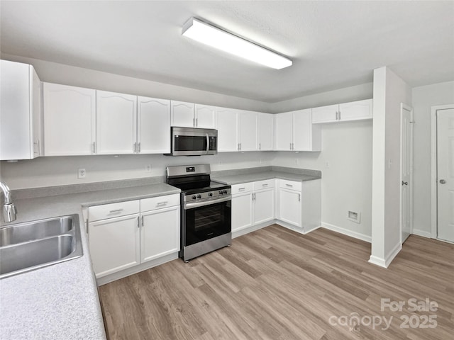 kitchen with light wood finished floors, a sink, white cabinetry, and appliances with stainless steel finishes
