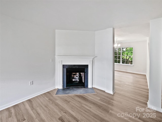 unfurnished living room featuring a premium fireplace, wood finished floors, baseboards, and an inviting chandelier