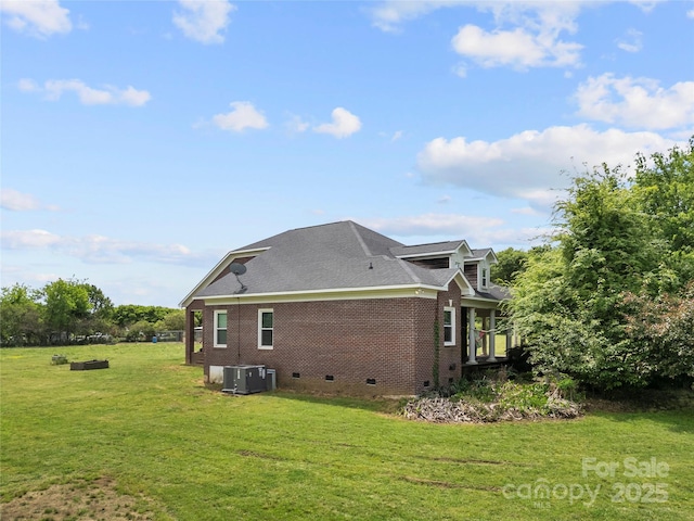 rear view of house featuring crawl space, brick siding, central air condition unit, a lawn, and a shingled roof