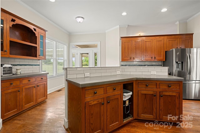kitchen with stainless steel fridge with ice dispenser, backsplash, brown cabinets, crown molding, and dark wood finished floors